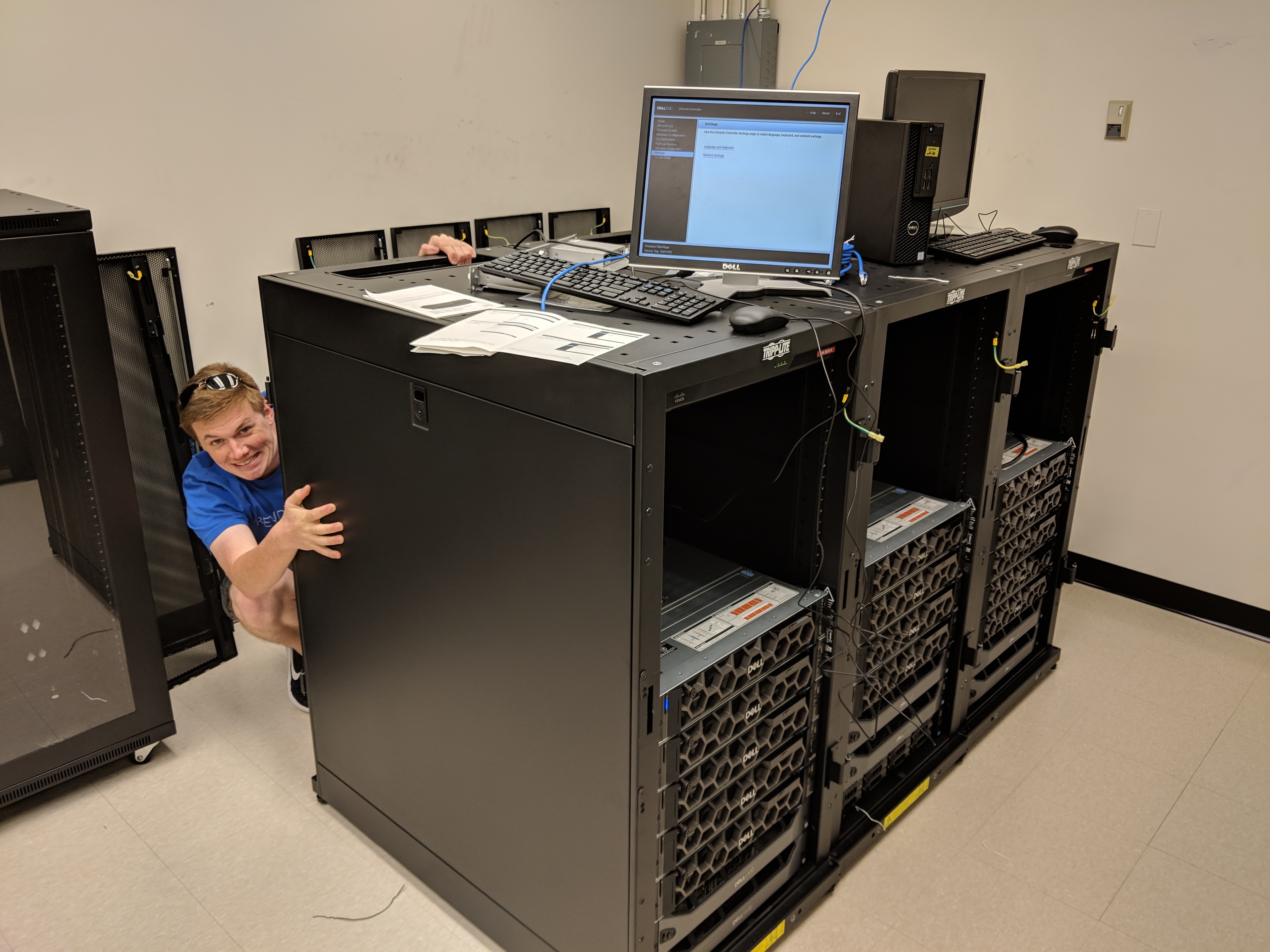 Messy room with server racks, with Chris hiding behind one of them